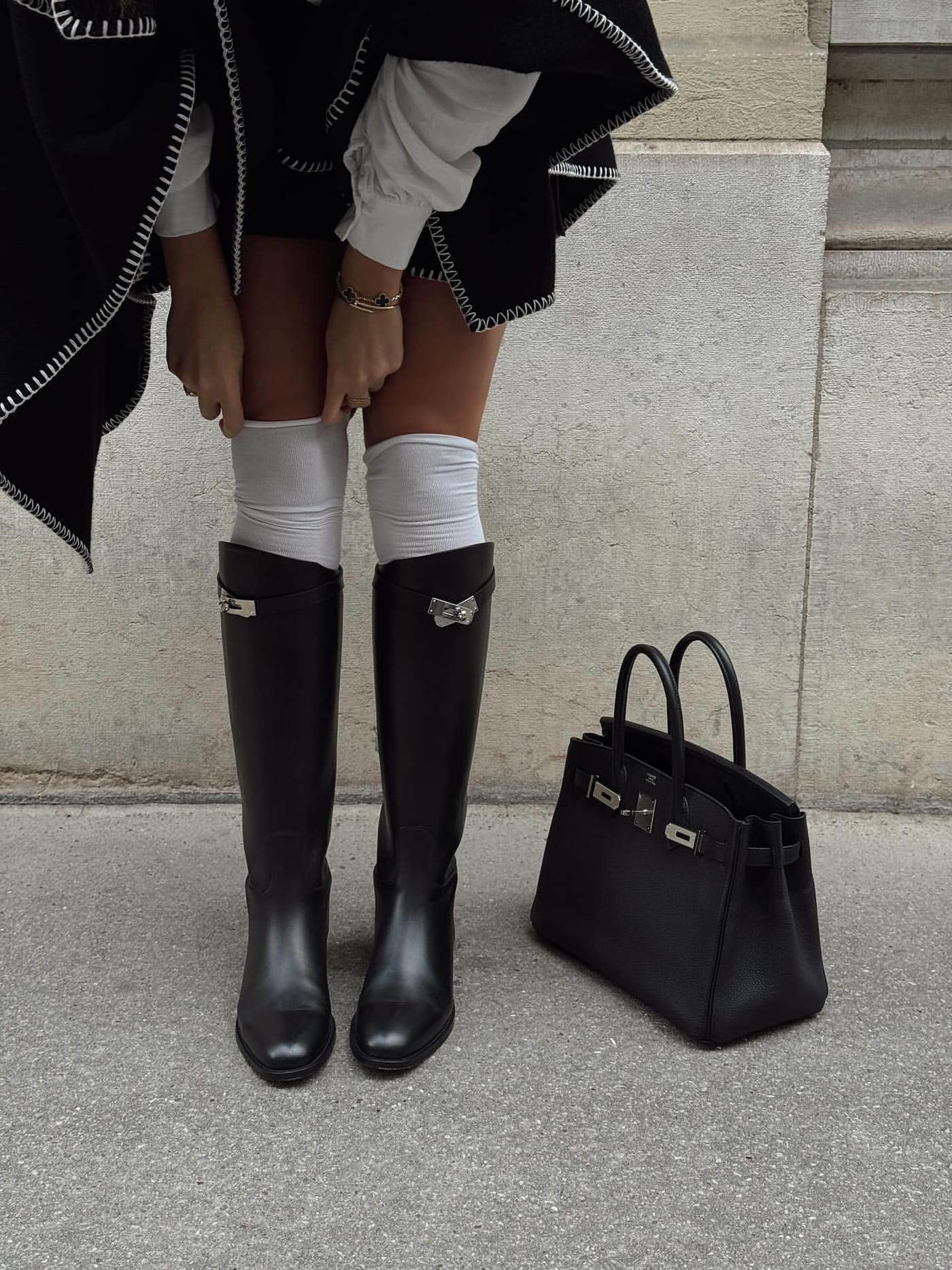 黑色 Jumping 長靴搭配白襪與斗篷，身旁放著黑色 Birkin。圖片：@limelightnova／PurseBop。